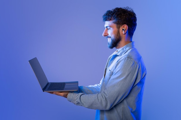 Un hombre con barba está de pie mientras sostiene una computadora portátil en sus manos parece estar mirando el