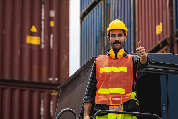 Hombre de barba de ingeniero de pie con un casco amarillo para controlar la carga y verificar la calidad de los contenedores del buque de carga para la importación y exportación en el astillero o puerto