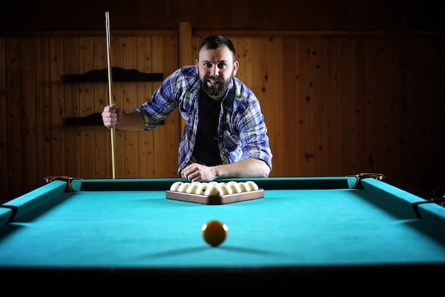 Un hombre con barba juega un gran billar. Fiesta en la piscina de 12 pies. Juego de billar en el club para hombres. Un hombre con taco rompe la pirámide.