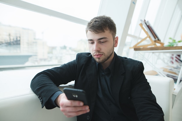 Hombre con barba mira el teléfono inteligente durante un descanso para almorzar en un café. Coffee break en un elegante café ligero.