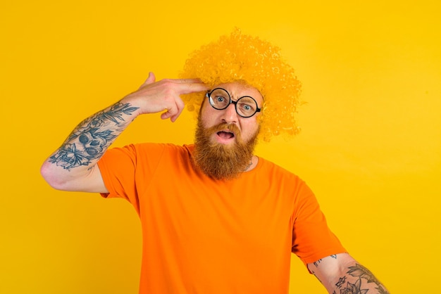 Hombre con barba peluca amarilla y gafas hace un gesto de pistola con la mano