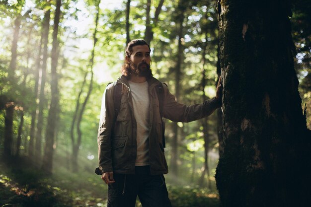 Foto hombre con barba de pie junto a un árbol en el bosque