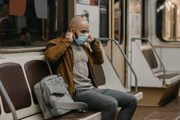 Un hombre con barba se pone una máscara médica en la cara para evitar la propagación del coronavirus en un vagón de metro. Un tipo calvo con una mascarilla quirúrgica contra COVID-19 está sentado en un tren del metro.