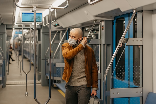 Un hombre con barba se pone una mascarilla médica para evitar la propagación del coronavirus en un vagón de metro. Un tipo calvo con una mascarilla quirúrgica contra COVID-19 mantiene distancia social en un tren.