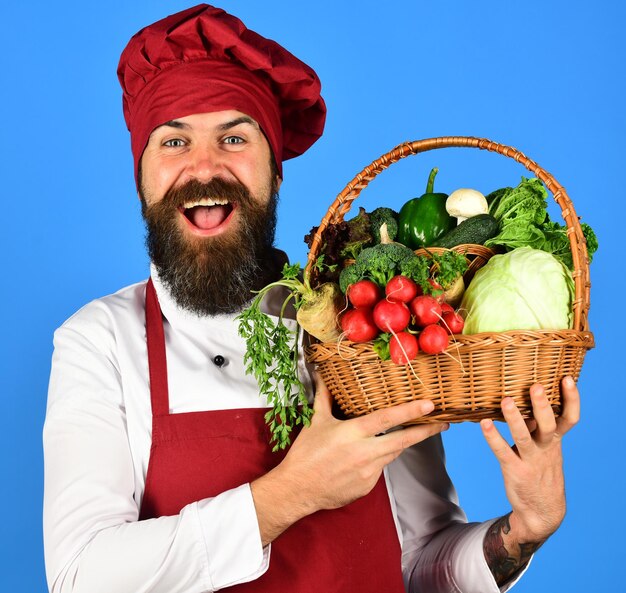 Hombre con barba sobre fondo azul Chef tiene verduras