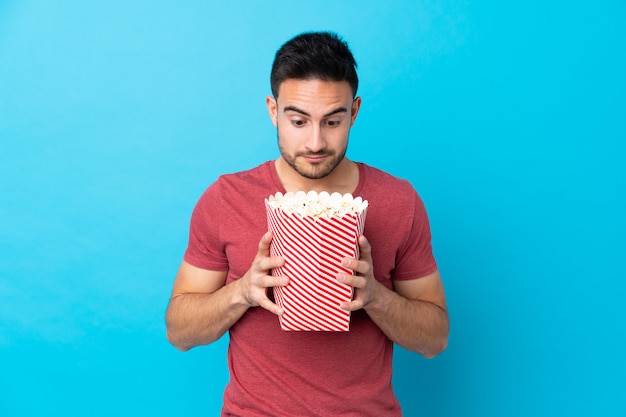 Hombre con barba sosteniendo una palomitas de maíz sobre pared aislada