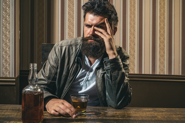 El hombre con barba sostiene brandy de vidrio. Hombre que sostiene un vaso de whisky. Hombre barbudo con estilo guapo está bebiendo en casa después del trabajo.