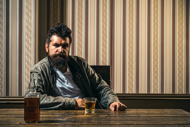 El hombre con barba sostiene brandy de vidrio. Hombre que sostiene un vaso de whisky. Hombre guapo con barba elegante es