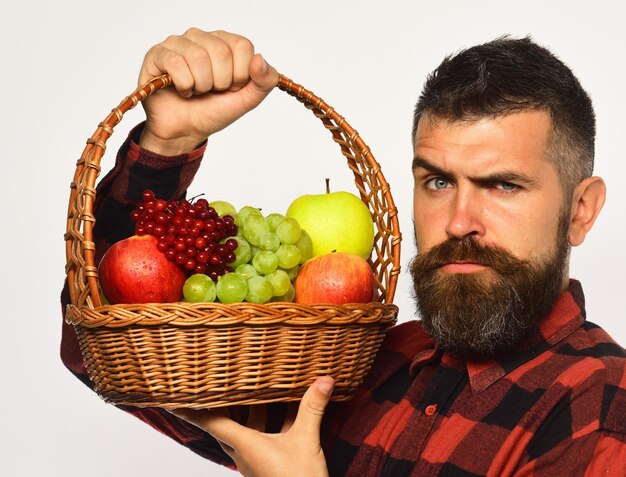 Hombre con barba sostiene cesta con fruta sobre fondo blanco.