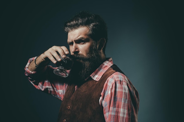 Hombre con barba sostiene una copa de brandy Hombre o hombre de negocios bebe whisky sobre fondo negro