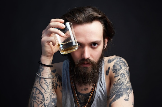 Hombre con barba y tatuaje bebe whisky