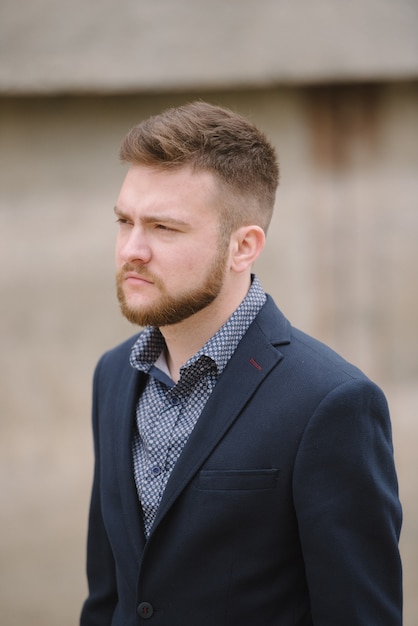 Un hombre con barba en traje azul posa en la calle para anunciar la ropa de los hombres.