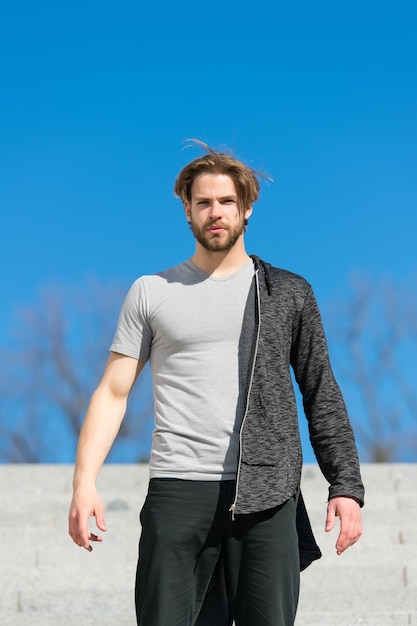 El hombre con barba usa una camiseta en la soleada moda al aire libre Macho se para en la perspectiva del cielo azul Moda y estilo para hombres Perspectiva de la libertad futura