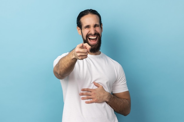 Foto hombre con barba vestido con camiseta blanca apuntando con el dedo índice a la cámara y riendo positivamente