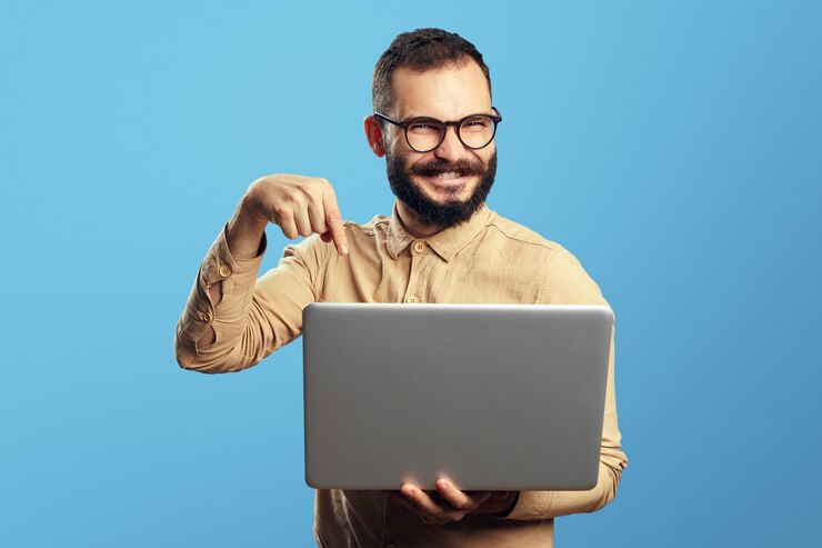 Hombre con barba viste camisa beige y puntos de anteojos en una nueva computadora portátil en