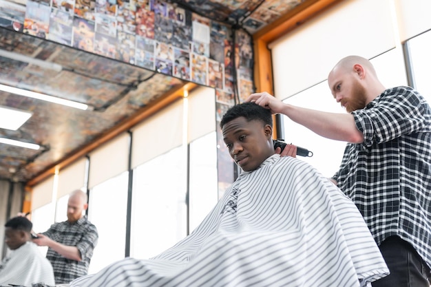 Hombre en la barbería Hombre negro guapo cortándose el pelo en un salón africano Peinado Corte de pelo para adultos