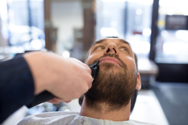 Foto hombre y barbero con cortador cortando la barba en el salón