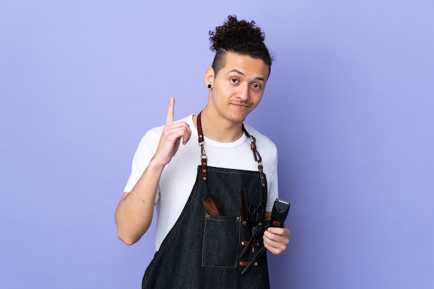 Hombre barbero en un delantal sobre pared púrpura aislada apuntando con el dedo índice una gran idea