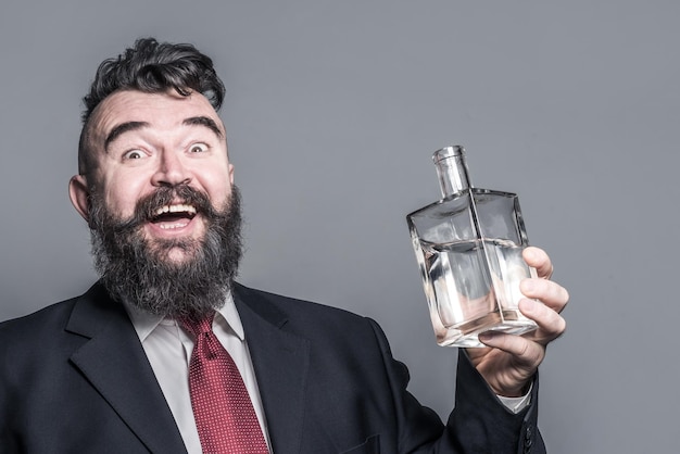 Hombre barbudo adulto feliz en traje sosteniendo una botella de alcohol a la luz del sol