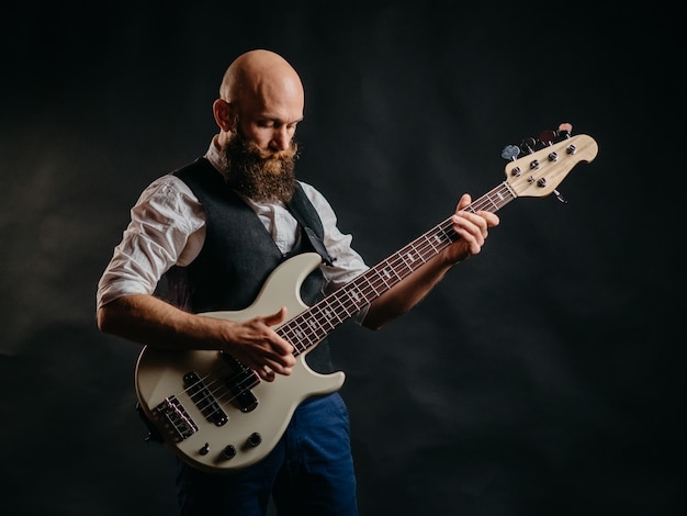 Hombre barbudo adulto tocando la guitarra con entusiasmo en un negro