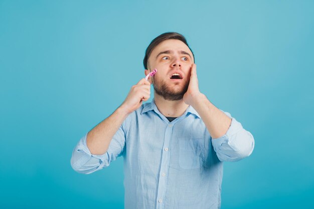 el hombre barbudo se afeita la maquinilla de afeitar rosa sobre fondo azul