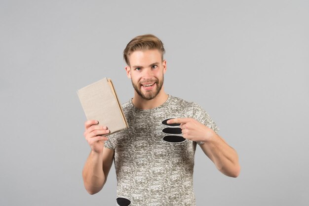 Hombre barbudo sin afeitar en camisa elegante apuntando al libro Hombre sonriente recomienda libro fondo gris Concepto de recomendación de literatura Hombre moderno escritor de moda libro publicado