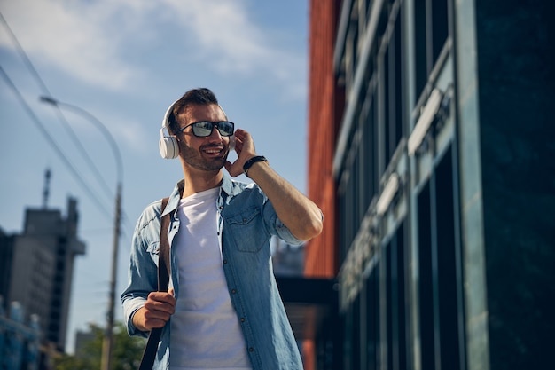 Hombre barbudo amable manteniendo una sonrisa en su rostro mientras disfruta de un paseo por el centro de la ciudad