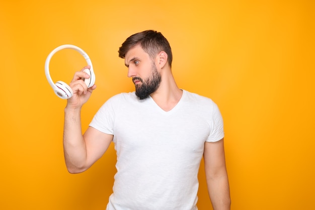 Hombre barbudo, amante de la música sostiene auriculares blancos frente a él.