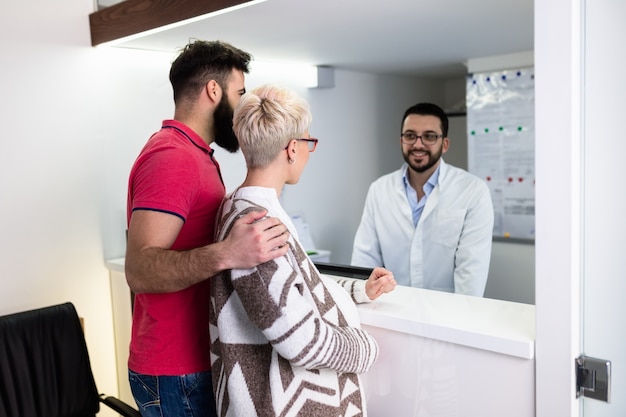 Hombre barbudo atractivo con su esposa embarazada con tratamiento médico en el consultorio dental.