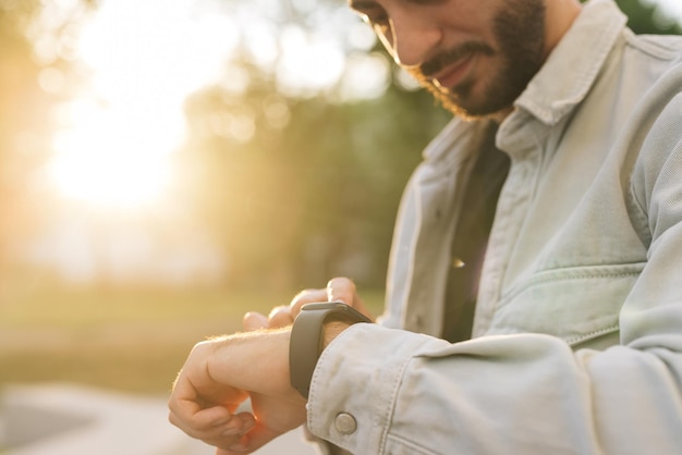Hombre barbudo de banda inteligente con tecnología portátil de pantalla táctil que usa un dispositivo de pulsera portátil con reloj inteligente
