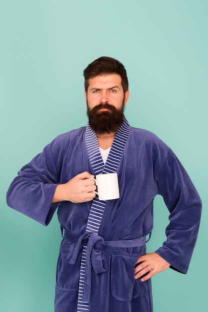 Foto hombre barbudo en bata de baño con taza concepto de desayuno hombre con barba en bata de baño azul disfruta del café o el té de la mañana chico en ropa de baño toma té café comienza un nuevo día cada mañana comienza con café