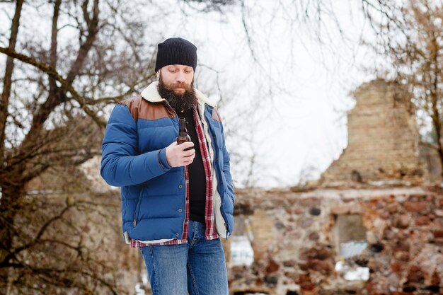 Hombre barbudo bebiendo cerveza en invierno en el bosque