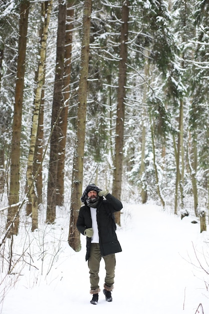 Hombre barbudo en el bosque de invierno. Atractivo joven feliz con barba caminar en el parque.