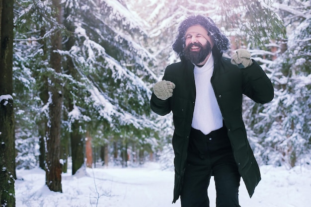 Hombre barbudo en el bosque de invierno. Atractivo joven feliz con barba caminar en el parque.