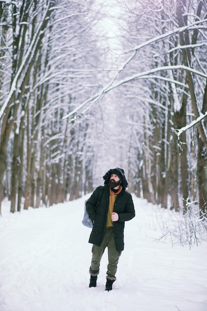 Hombre barbudo en el bosque de invierno. Atractivo joven feliz con barba caminar en el parque.