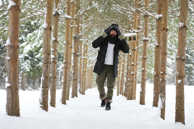 Hombre barbudo en el bosque de invierno. Atractivo joven feliz con barba a pie en el parque.