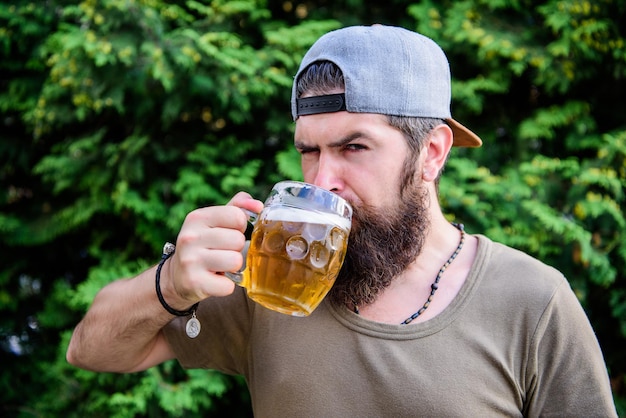 Hombre barbudo brutal hipster sostenga una taza de cerveza fría y fresca La cerveza artesanal es joven, urbana y de moda Concepto de cerveza y cerveza Hombre relajante disfrutando de la cerveza Día caluroso de verano Saciar la sed Bebida de alcohol y bar