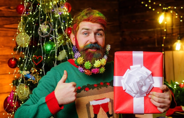 Hombre barbudo con caja de regalo presente que muestra el pulgar hacia arriba le deseo feliz navidad vacaciones de año nuevo