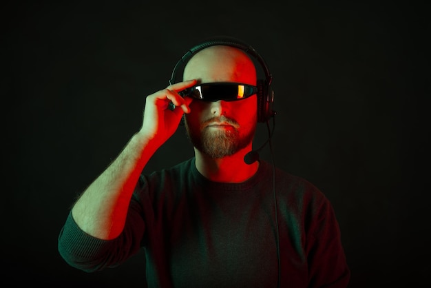 Hombre barbudo calvo con auriculares y gafas de cíclope sobre fondo negro Foto de estudio con luz roja