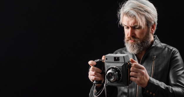 Hombre barbudo con cámara de fotos Vintage. Fotógrafo elegante en chaqueta de cuero con cámara retro.