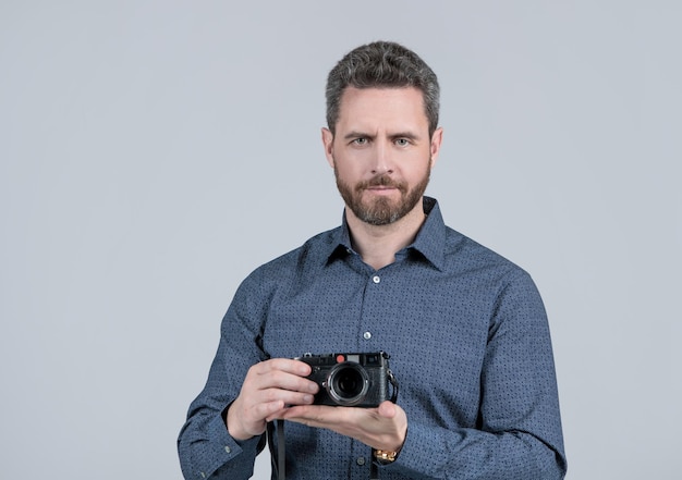 Hombre barbudo con camisa de estilo informal sostenga la cámara fotográfica del telémetro sobre fondo gris a mano, fotografía.