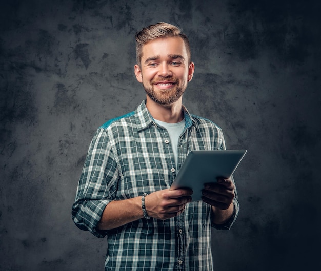 Hombre barbudo en una camisa de lana tiene tablet PC sobre fondo gris.