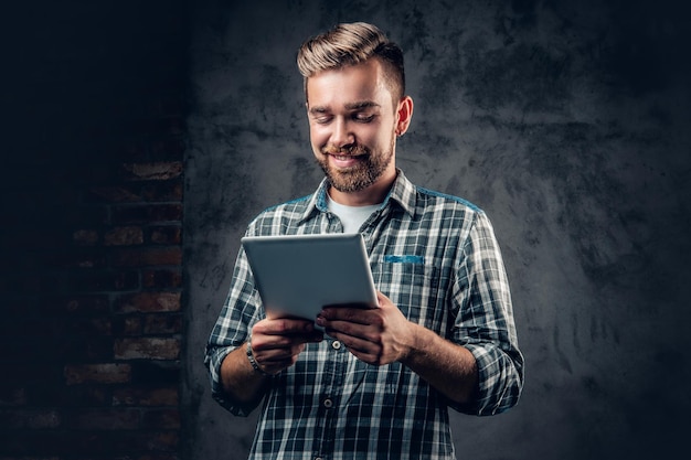 Foto hombre barbudo en una camisa de lana tiene tablet pc sobre fondo gris.