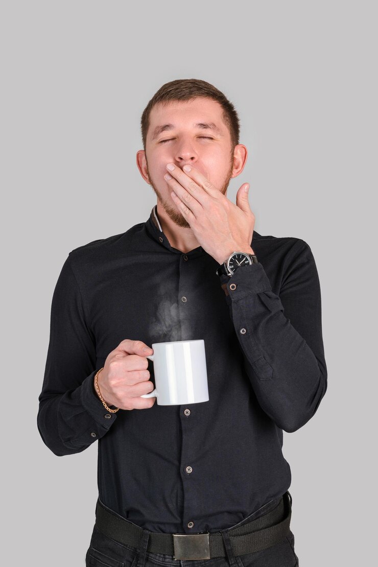 Un hombre barbudo con una camisa negra bosteza con una taza blanca en la mano, foto vertical