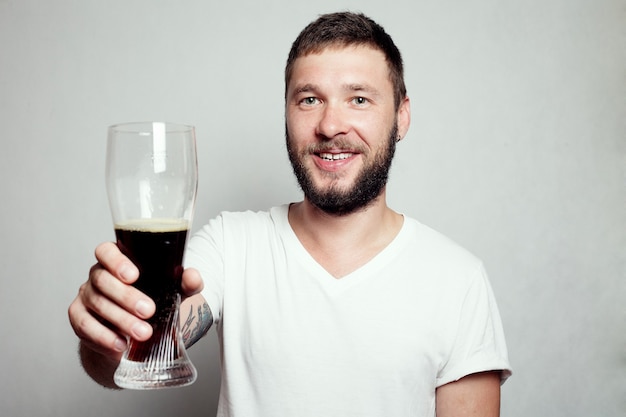 Hombre barbudo con una camiseta blanca sosteniendo un vaso de pinta