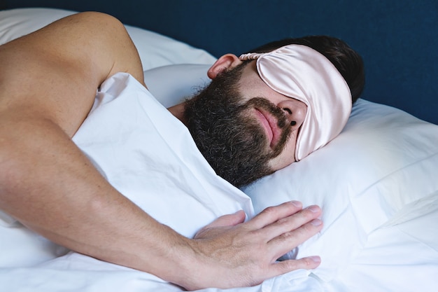 Hombre barbudo caucásico en máscara para los ojos durmiendo en la cama