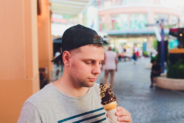 Hombre barbudo corto comiendo helado en una calle de la ciudad.