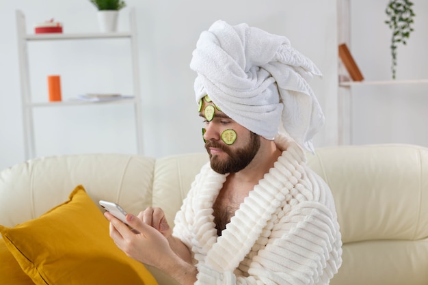 Hombre barbudo disfruta con una mascarilla cosmética en su rostro hecha de rodajas de pepino y cuidado de la piel de los hombres