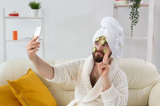 Hombre barbudo divertido con rodajas de pepino en la cara. Spa en casa, cuidado del cuerpo y de la piel por concepto masculino.