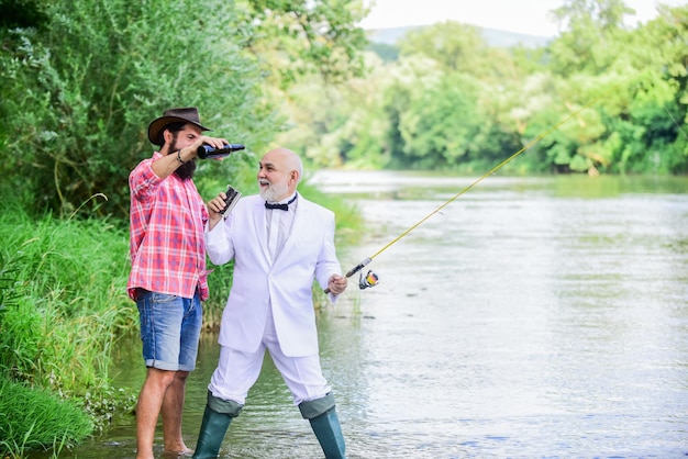 Hombre barbudo y elegante hombre de negocios pescando juntos Hombres relajantes en el fondo de la naturaleza Diversión y relajación Tiempo de fin de semana Habilidades de pesca Montar caña con anzuelo y plomo Pescar y beber cerveza